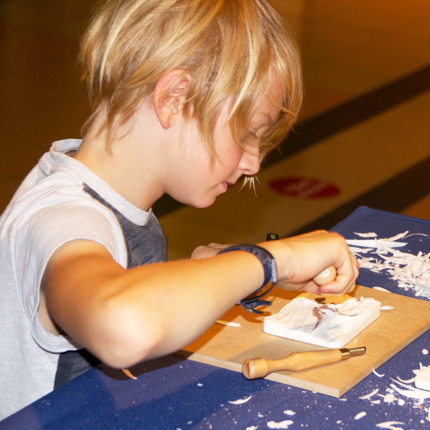 Ein 9-jähriger Schnitzanfänger schnitzt ein 3D Dino-Skelett mit einem Hohlbeitel. Er lernt die Arbeit mit dem Werkzeug durch konzentriertes Arbeiten mit dem neuartigen Material Kartoffelholz. 